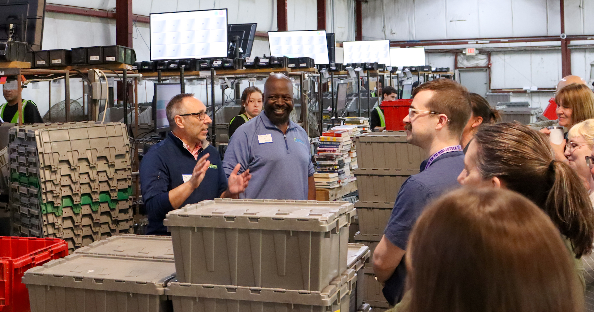 Two Optima Shipping employees smiling and speaking to a group of people gathered around sorting bins.